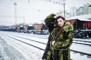 chica morena con abrigo de piel verde en la estación de la plataforma en el día de invierno. foto