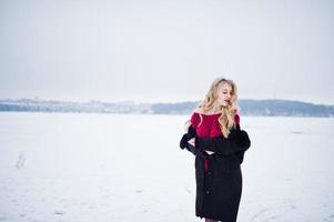 Elegance blonde girl in fur coat and red evening dress posed at winter snowy day. photo