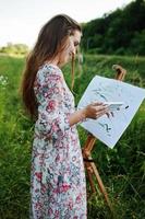 Portrait of an attractive young woman in long dress painting with watercolor in nature. photo