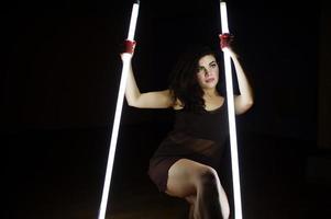 Curly brunette plus size model with two long led lamp at black room. photo