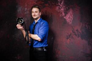 Studio portrait of stylish professional photographer man with camera, wear on blue shirt and necktie. photo