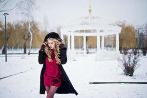 Elegance blonde girl in fur coat and red evening dress posed at winter snowy day. photo