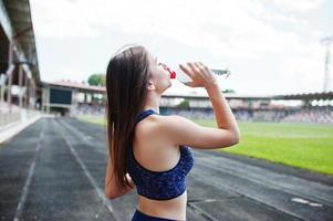 Portrait of a fit woman drinking water after running in the stadium. photo