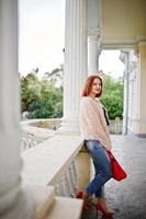 Red haired girl with red handbag posed near vintage house. photo