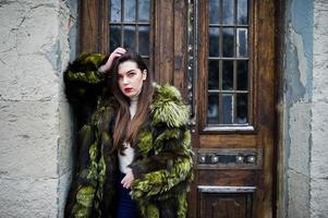 Brunette girl in green fur coat against old wooden doors. photo