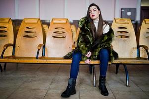 Brunette girl in green fur coat on the chairs in the waiting room at the station. photo