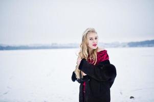 chica rubia de elegancia en abrigo de piel y vestido de noche rojo posó en el día de nieve de invierno. foto