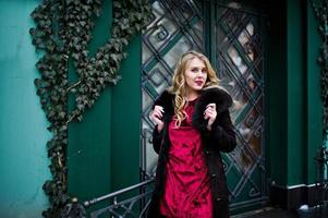 Elegance blonde girl in red evening dress and fur coat at streets of city. photo