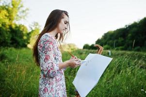 Portrait of an attractive young woman in long dress painting with watercolor in nature. photo