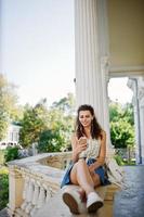 Curly stylish girl wear on blue jeans skirt, blouse posed near old vintage house. photo