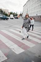 chica de abrigo gris con gafas de sol y bolso caminando por el paso de peatones. foto