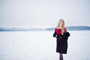 Elegance blonde girl in fur coat and red evening dress posed at winter snowy day. photo