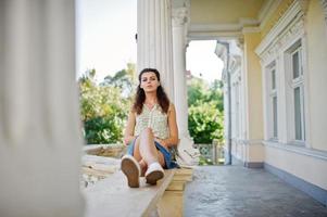 Curly stylish girl wear on blue jeans skirt, blouse posed near old vintage house. photo