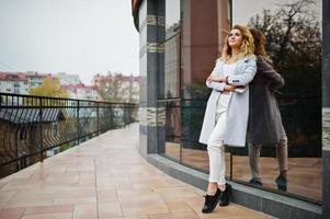 Stylish curly blonde model girl wear on white with mobile phone at hand posing against large window. photo