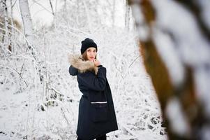 Beautiful brunette girl in winter warm clothing. Model on winter jacket and black hat. photo