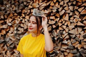 Young funny girl with bright make-up, like fairytale princess, wear on yellow shirt and crown against wooden background. photo