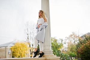 Stylish curly blonde model girl wear on white posing against old vintage house. photo