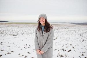 Gentle girl in gray coat and hat against snow landscape.