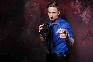 Studio portrait of stylish professional photographer man with camera, wear on blue shirt and necktie. photo