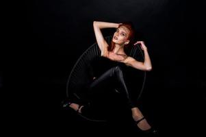 modelo de moda chica pelirroja con maquillaje original como depredador leopardo aislado en negro. retrato de estudio en silla. foto