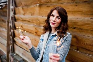 Portrait of brunette girl in jeans jacket with bengal lights in hands. photo