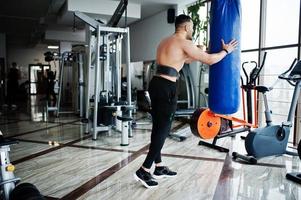 Muscular arab man training in modern gym. Fitness arabian men with naked torso doing exercises with boxing bag. photo