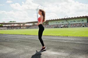 Fitness sporty girl in sportswear at a football stadium outdoor sports. Happy sexy woman workout and jumping with rope. photo