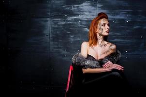 Fashion model red haired girl with originally make up like leopard predator against steel wall. Studio portrait on ladder. photo