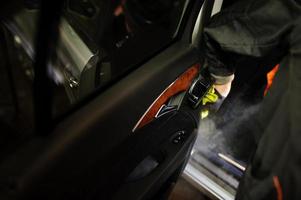 Man in uniform and respirator, worker of car wash center, cleaning car interior with hot steam cleaner. Car detailing concept. photo