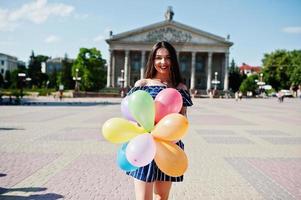 hermosa chica morena en la calle de la ciudad con globos en las manos. foto