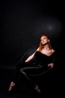 Fashion model red haired girl with originally make up like leopard predator isolated on black. Studio portrait on chair. photo