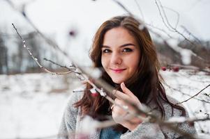 Close up portrait of gentle girl in gray coat near the branches of a snow-covered tree. photo