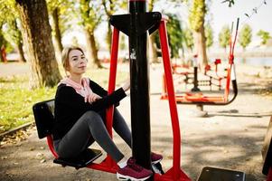 la joven tiene el entrenamiento y hace ejercicio al aire libre en simuladores callejeros. deporte, fitness, concepto de entrenamiento callejero. foto