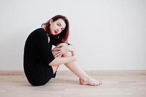 Red haired girl on black dress tunic against white wall at empty room. photo