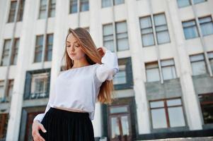 Portrait of a fabulous young successful woman in white blouse and broad black pants posing on the stairs with a huge white building on the background. photo