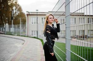 Elegant blonde girl wear on black posing at streets of town against iron cage. photo