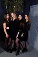 Four cute friends girls wear black dresses against christmas decoration. photo