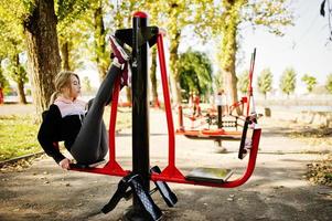 Young girl has the training and doing exercise outdoors on street simulators. Sport, fitness, street workout concept. photo