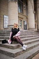 chica rubia con gafas y abrigo rosa con bolso sentado en las escaleras del edificio de la ópera. foto