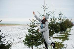 Portrait of gentle girl in gray coat and hat against new year tree outdoor. photo