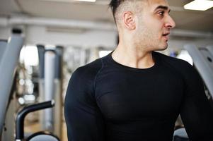 hombre árabe musculoso entrenando y haciendo ejercicio en una máquina de fitness en un gimnasio moderno. foto