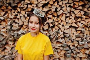 Young funny girl with bright make-up, like fairytale princess, wear on yellow shirt and crown against wooden background. photo