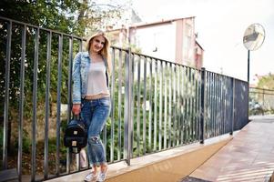 chica rubia vestida con jeans con mochila posada en la calle. foto