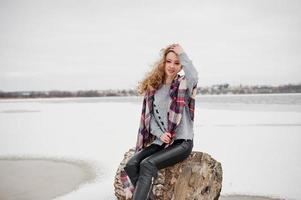 chica rubia rizada en tela escocesa a cuadros contra el lago congelado en el día de invierno. foto