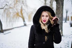 Elegance blonde girl in fur coat and red evening dress posed at winter snowy day. photo