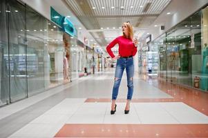 Portrait of a gorgeous woman in red blouse and jeans holding a cup of coffee in a shopping mall. photo