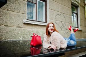 Red haired girl with red handbag posed at street of city. photo