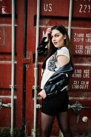 Stylish brunette girl wear on leather jacket and shorts against shipping container. photo