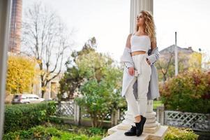 Stylish curly blonde model girl wear on white posing against old vintage house. photo