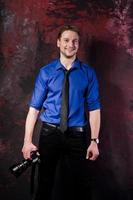 Studio portrait of stylish professional photographer man with camera, wear on blue shirt and necktie. photo